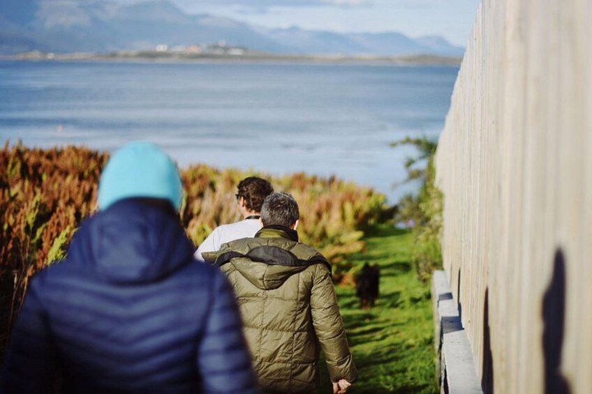 A group of people walking along a path beside a body of water with mountains in the background. 3