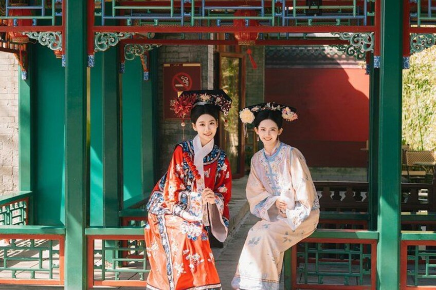 Two individuals in traditional Chinese attire standing in front of a green and red architectural structure with intricate designs. 4