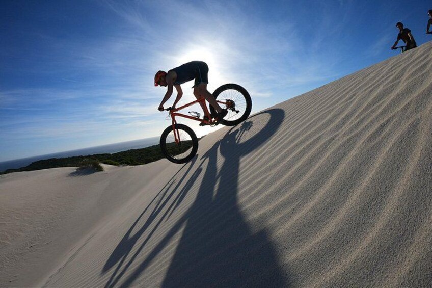 En person cykler op ad en sandskråning med solen i baggrunden. 4