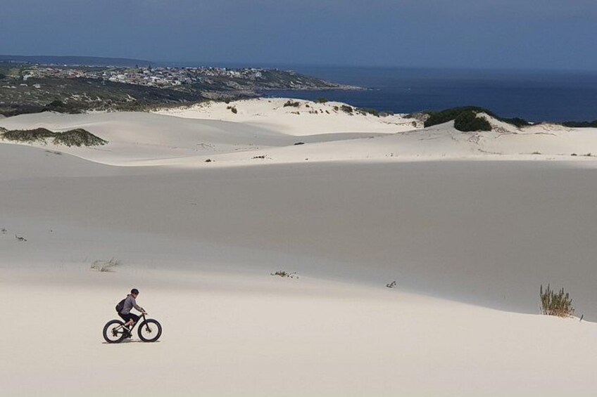 En person cykler på en sandklit med et kystlandskab i baggrunden. 3