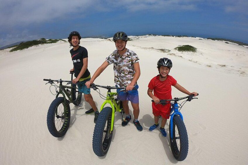 Tre personer på en sandstrand med cykler. 2