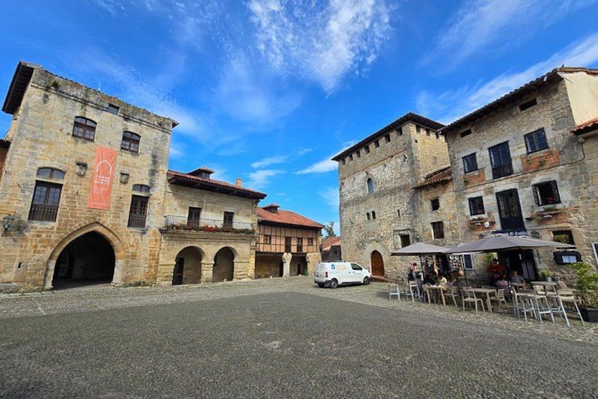 A historic square with stone buildings, a white van, and outdoor seating. 3