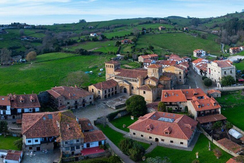 A village with red-roofed buildings, a central square, and surrounding green hills. 1