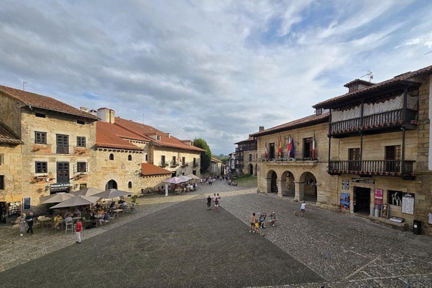 A cobblestone square with historic buildings, a central archway, and outdoor seating areas. 5