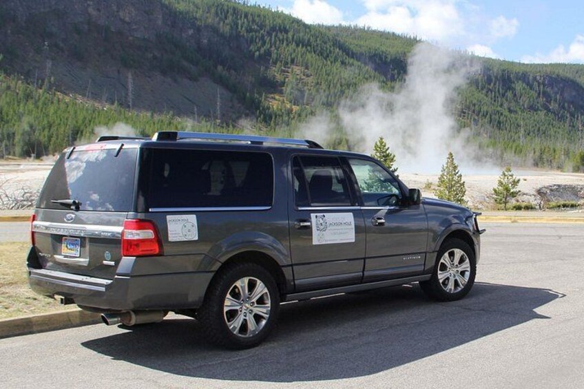 A gray SUV parked on a road with a mountainous background and steam rising from the ground. 5