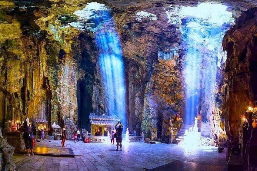 Een grot met een waterval, verlicht met kunstlicht, en een traditioneel gebouw aan de voet ervan. 4