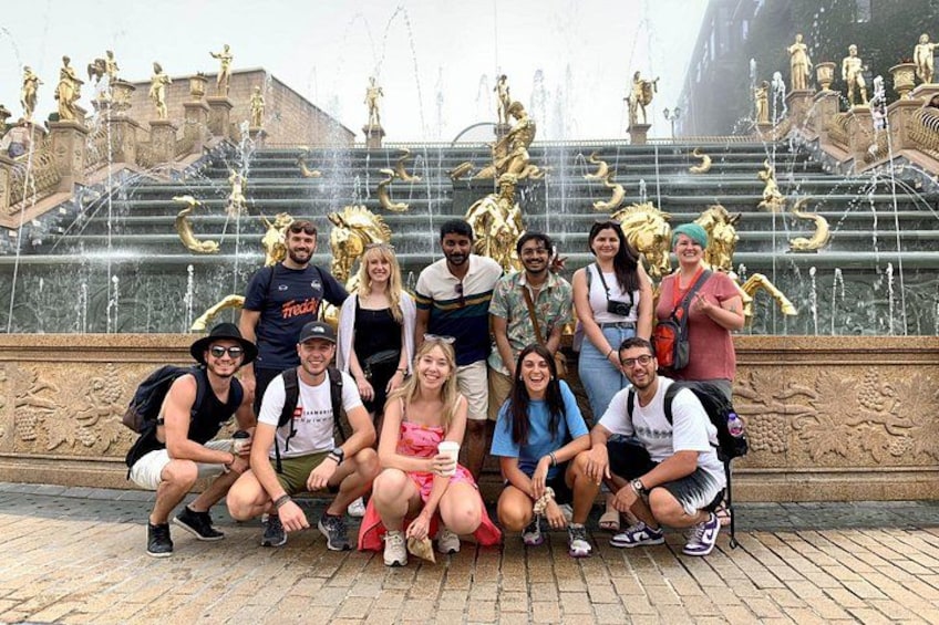 Een groep mensen die poseert voor een fontein met beelden en waterstralen. 2