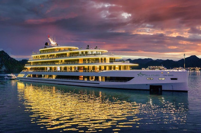 A multi-deck yacht named 'Sea Stars' with a lit-up facade, docked at a marina with mountains in the background. 3