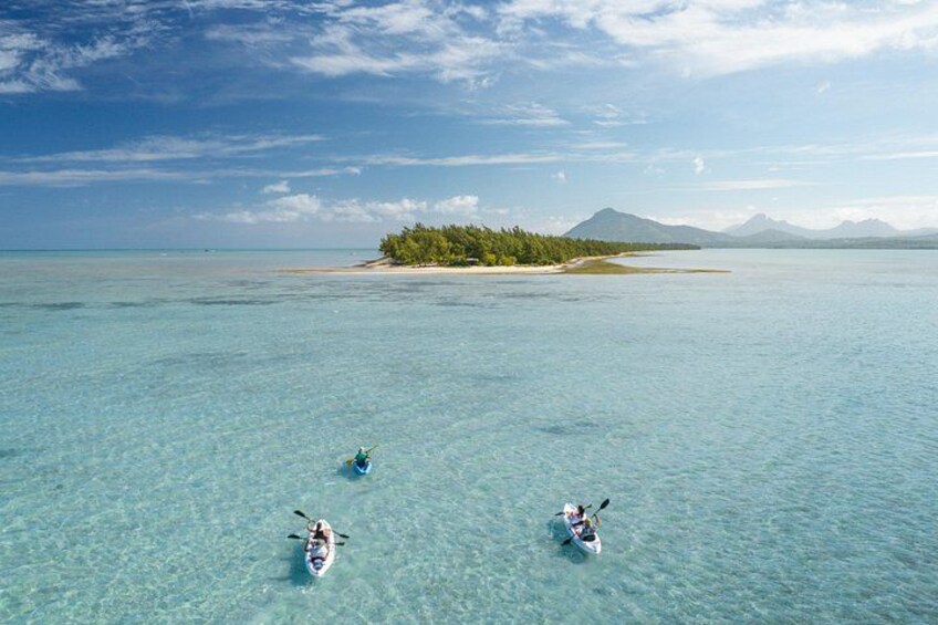 Three kayaks on clear turquoise water with a small island and mountains in the background. 1