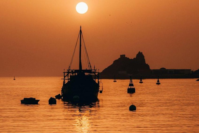 A sunset over a calm sea with a large ship and several smaller boats. 3