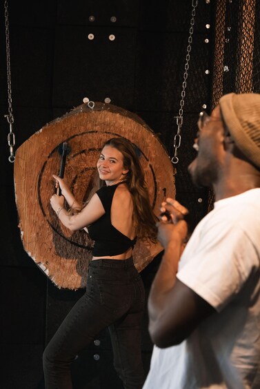 A person holding a microphone, standing in front of a large wooden sign with chains. 2