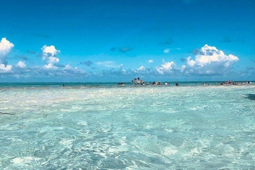 A beach with clear turquoise water, a few people in the distance, and a clear sky. 2