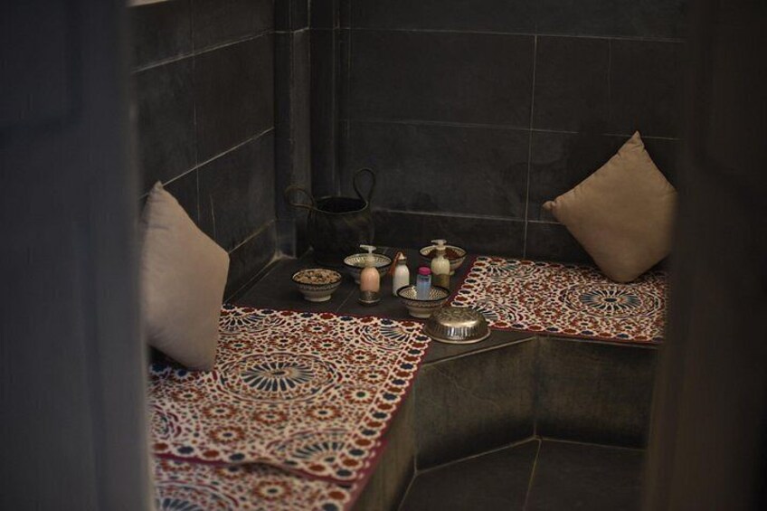 Un baño de estilo marroquí con paredes de azulejos, una alfombra estampada y una pequeña mesa con adornos. 3