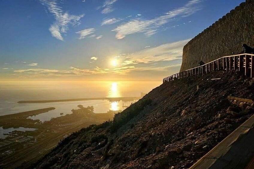 Un paysage côtier avec un grand mur, un coucher de soleil et une étendue d’eau calme. 3