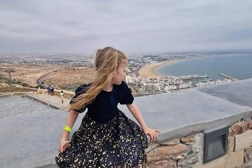A person standing on a high vantage point overlooking a coastal cityscape with a beach and a clear view of the sea. 4
