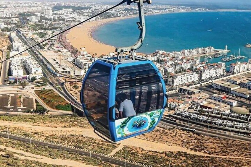 A cable car with a passenger, a coastal cityscape, and a beach. 3