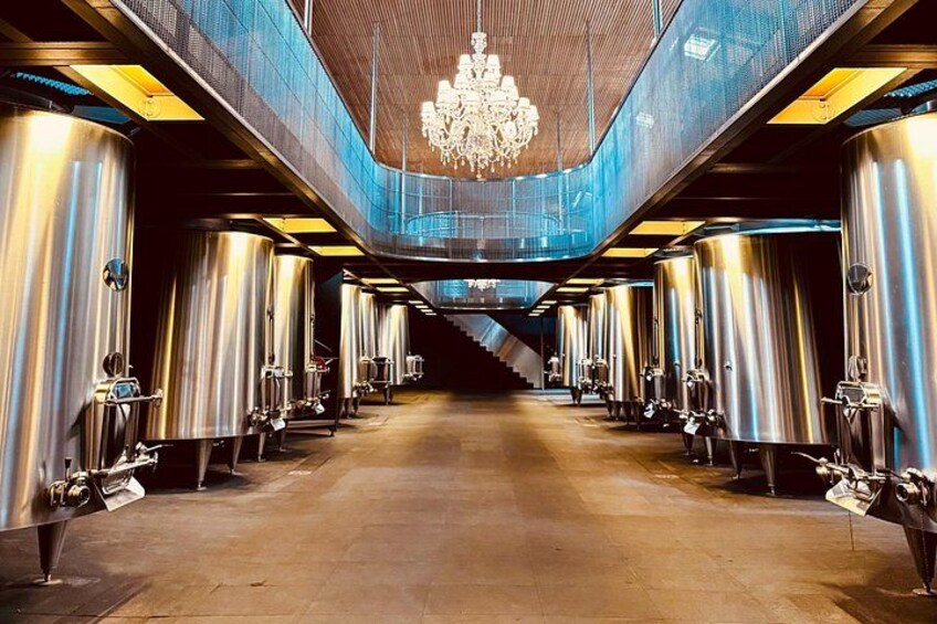 A row of stainless steel fermentation tanks in a brewery with a chandelier hanging from the ceiling. 3