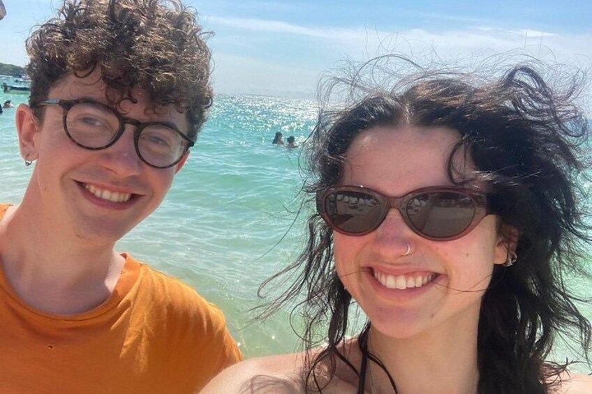 Dos personas en la playa, con agua cristalina y otras personas al fondo. 5