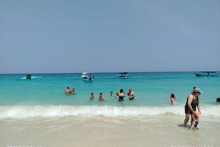 Una playa con gente nadando y barcos en el agua. 3