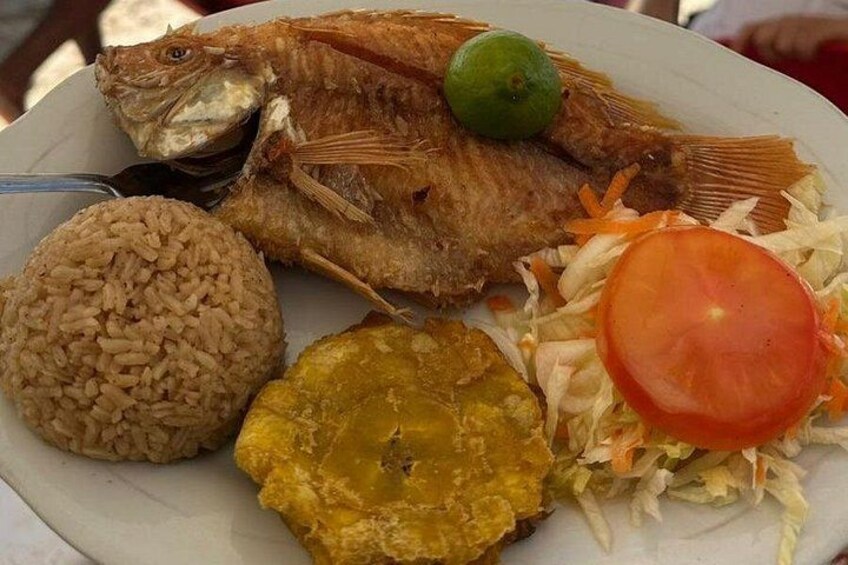 Un plato con pescado frito, arroz, plátanos fritos y una rodaja de tomate. 4
