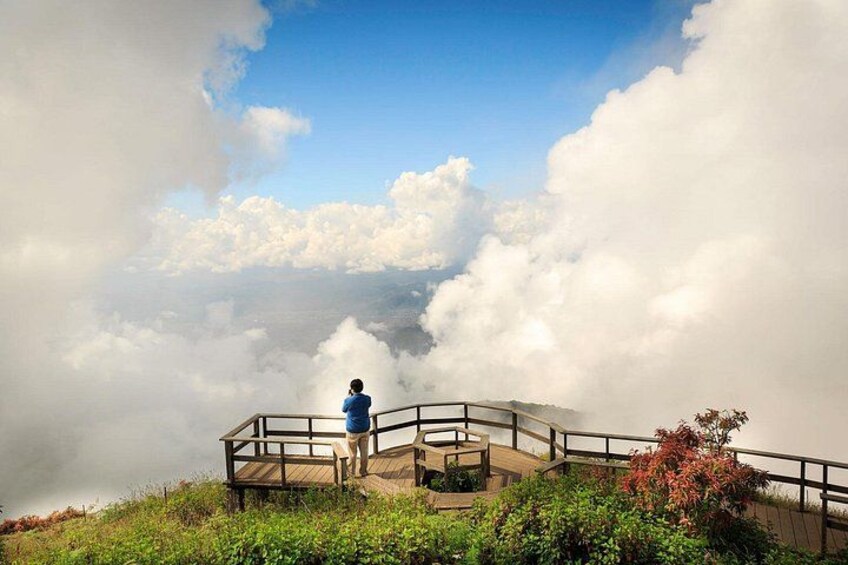A person standing on a wooden platform overlooking clouds. 1
