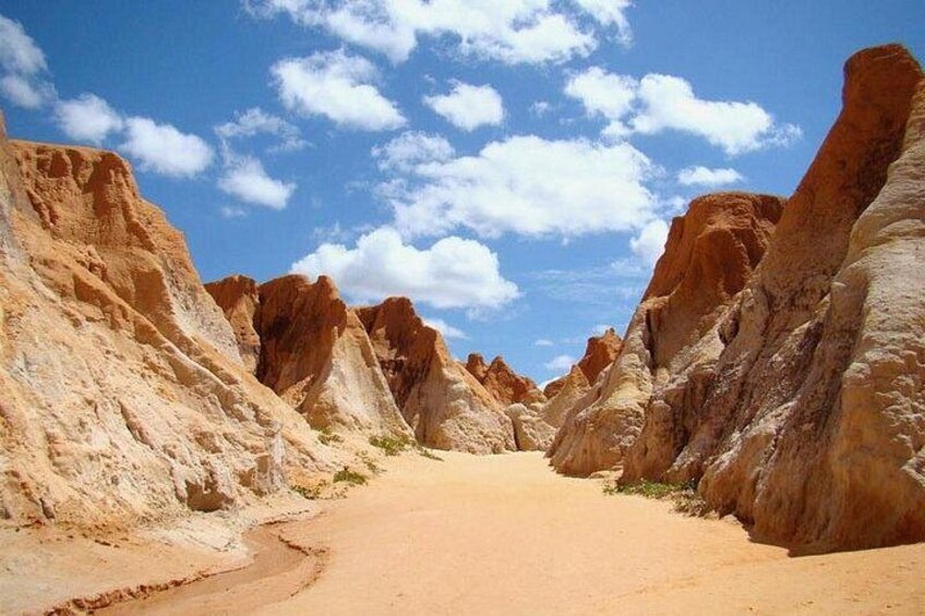 A desert landscape with a winding dirt road, towering rock formations, and a clear blue sky. 2