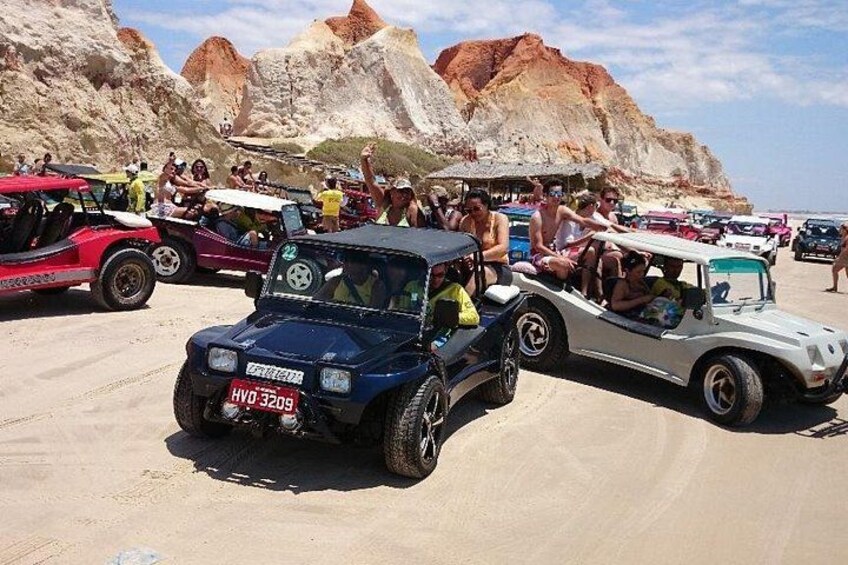 A desert landscape with rocky formations and a group of off-road vehicles parked on the sand. 3