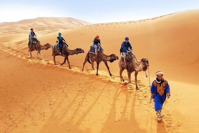 A group of people riding camels across a desert landscape. 1