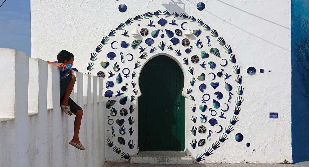 A child climbing a white wall with a circular pattern of handprints and a green door. 1