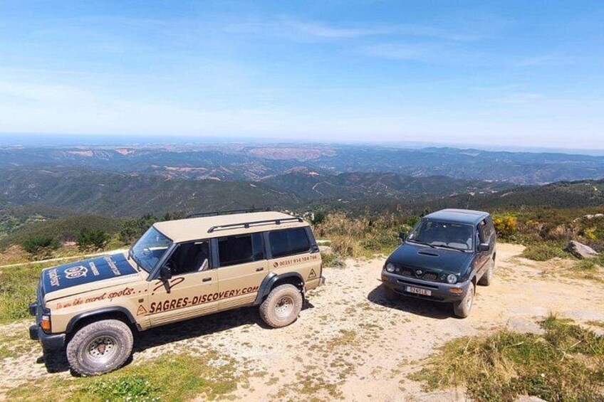 Two off-road vehicles parked on a dirt path with a mountainous landscape in the background. 2
