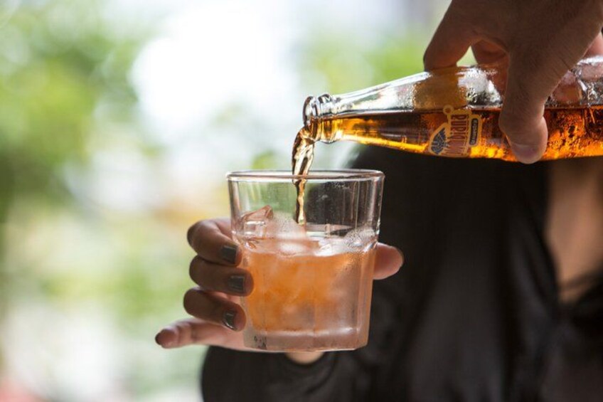 En person häller en mörk vätska från en flaska i ett genomskinligt glas. 2