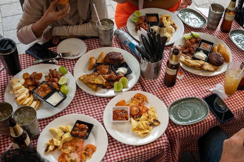 A group of people sitting at a table with various dishes, drinks, and condiments. 4