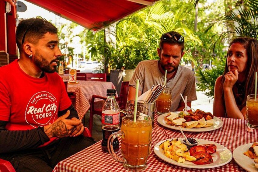A group of people dining outdoors at a restaurant with a red and white checkered tablecloth. 2