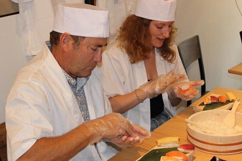 Two people wearing chef hats and gloves preparing food at a table. 5