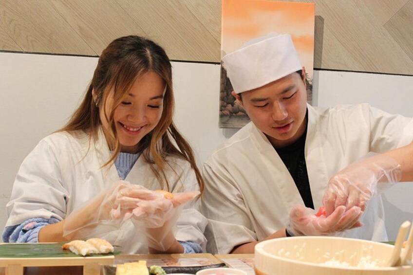 Two people in white chef uniforms preparing food, with a bowl of rice and some vegetables on the table. 4