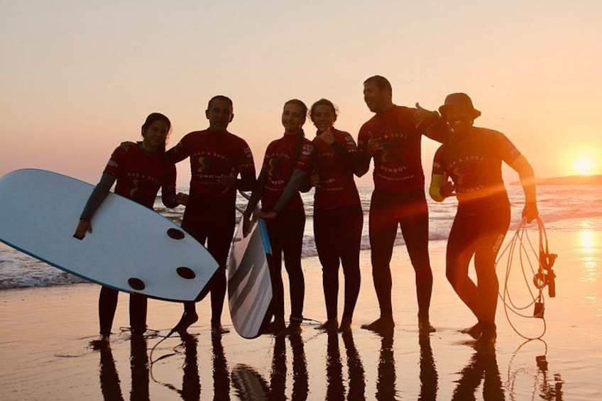 Een groep mensen op het strand bij zonsondergang, sommigen met surfplanken. 5