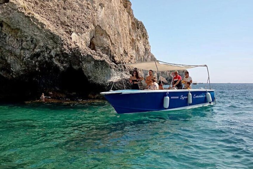 Ein blaues Boot mit Passagieren in der Nähe einer steilen Klippe. 1