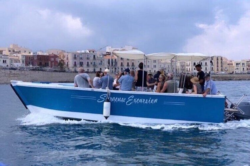A blue boat named 'Enrique Excursion' with people on board, sailing on water with buildings in the background. 3