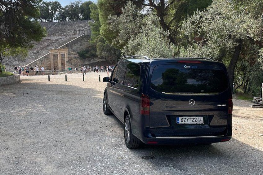 Un vehículo estacionado en un área de estacionamiento, con una estructura de piedra y árboles al fondo. 2