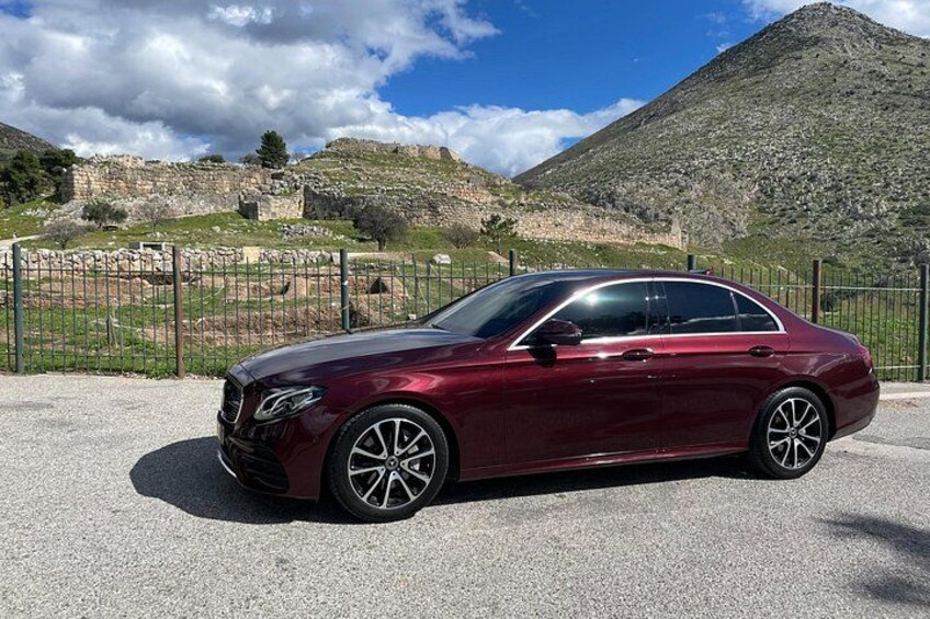 Un sedán color caoba estacionado sobre grava, con un paisaje montañoso al fondo. 3