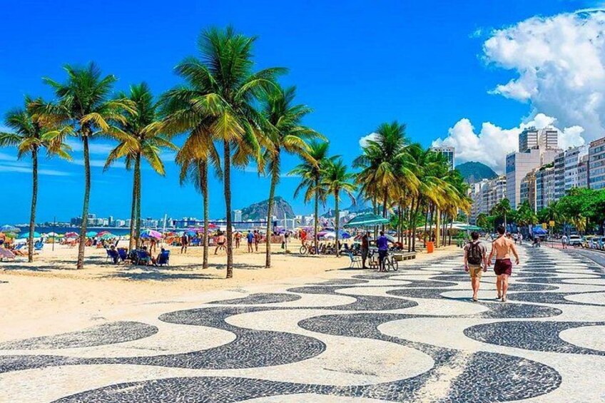 Una playa con palmeras, gente caminando y un paseo con baldosas. 3