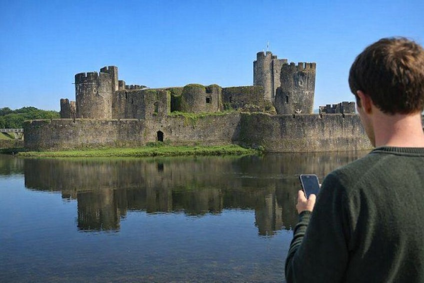 A historic castle with a moat, a person taking a photo, and a clear blue sky. 1