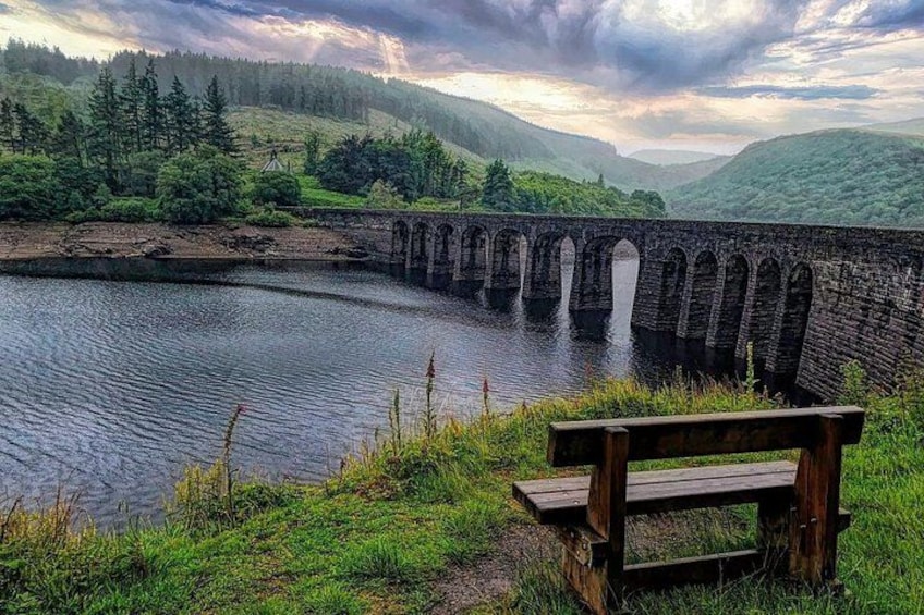 A stone bridge over a river, surrounded by greenery and hills. 3