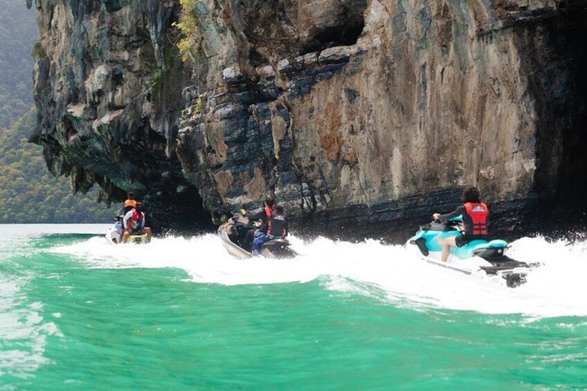 Tre persone su jet ski vicino a una scogliera rocciosa. 1