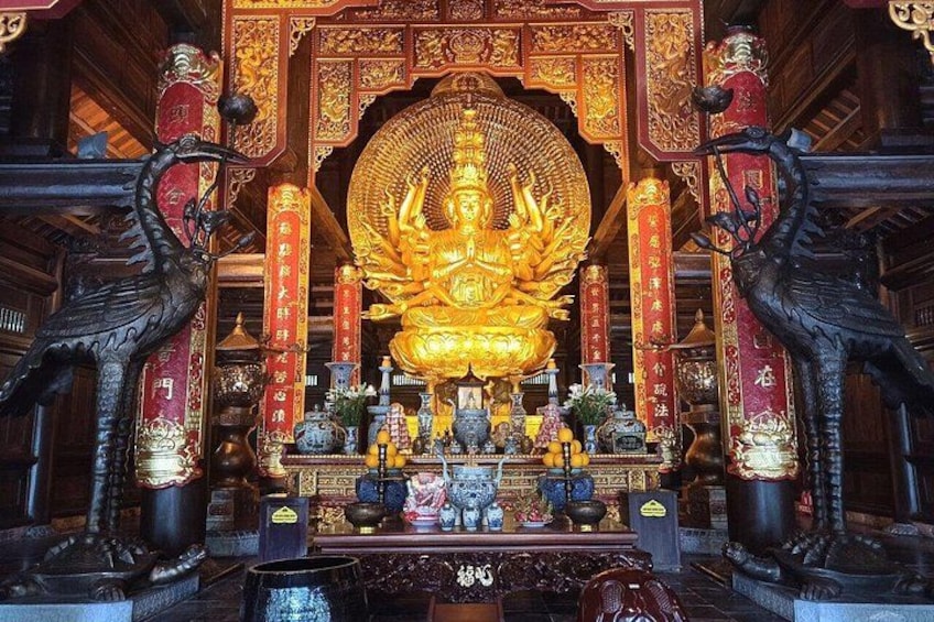 Eine goldene Statue mit aufwendigen Verzierungen, umgeben von roten und goldenen Dekorationen, mit je einer schwarzen Statue auf jeder Seite. 2