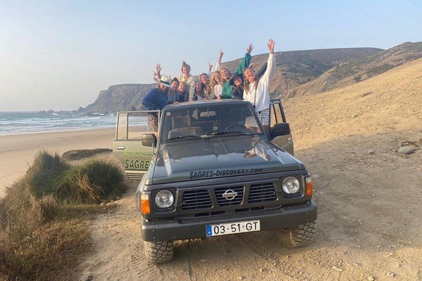 Un groupe de personnes se trouve dans un véhicule sur une plage, avec un paysage rocheux en arrière-plan. 3