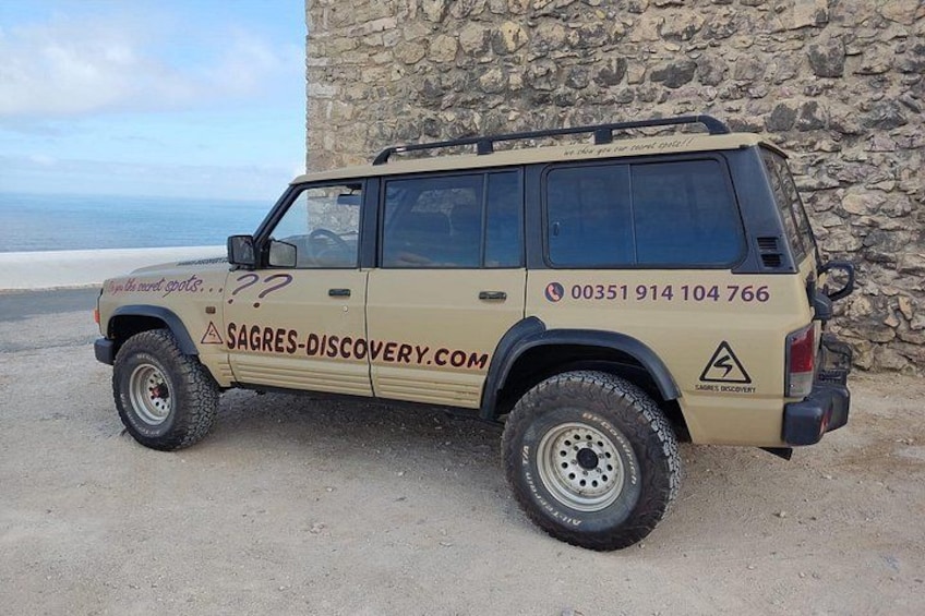 En beige terrängbil står parkerad nära en stenmur vid havet. 2