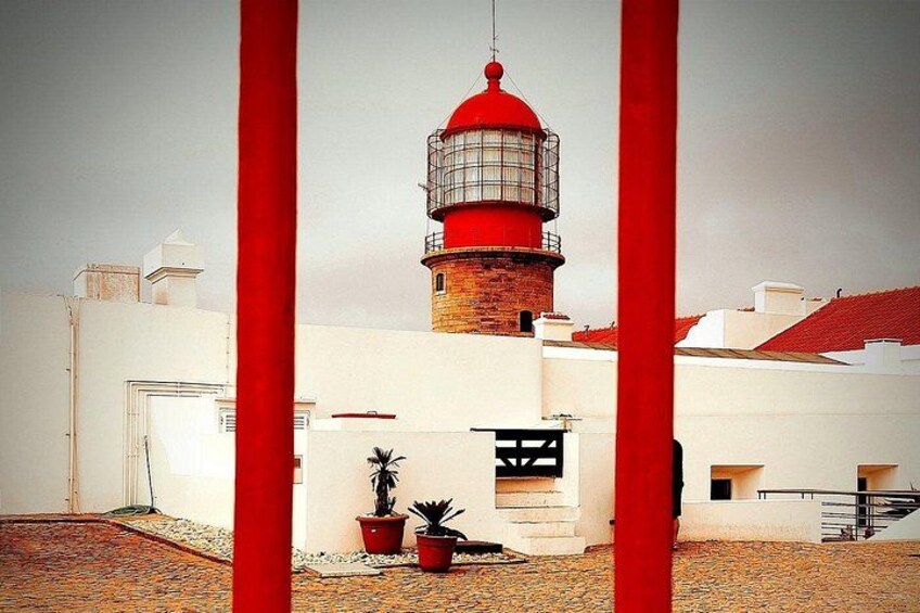 Un phare coiffé d’un dôme rouge, entouré de bâtiments blancs et de colonnes rouges. 2
