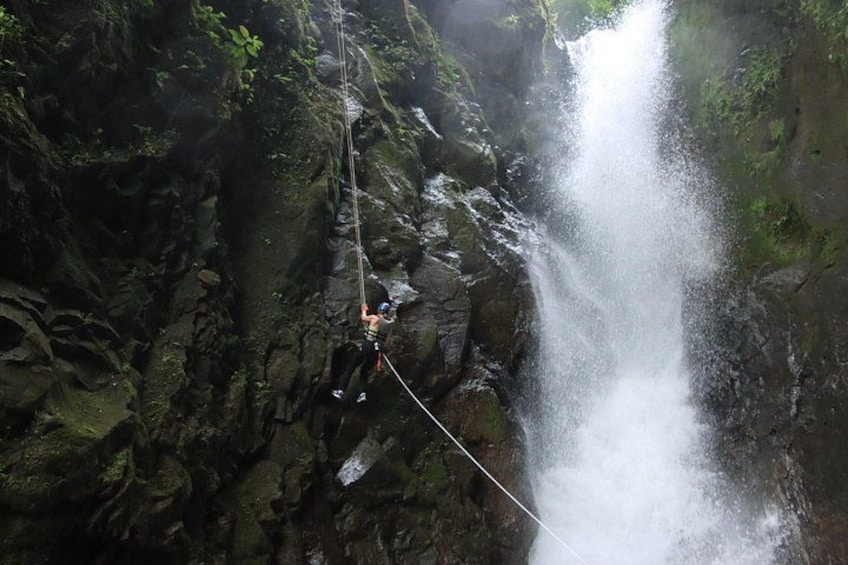 A person rappelling down a rocky cliff with a waterfall in the background. 4