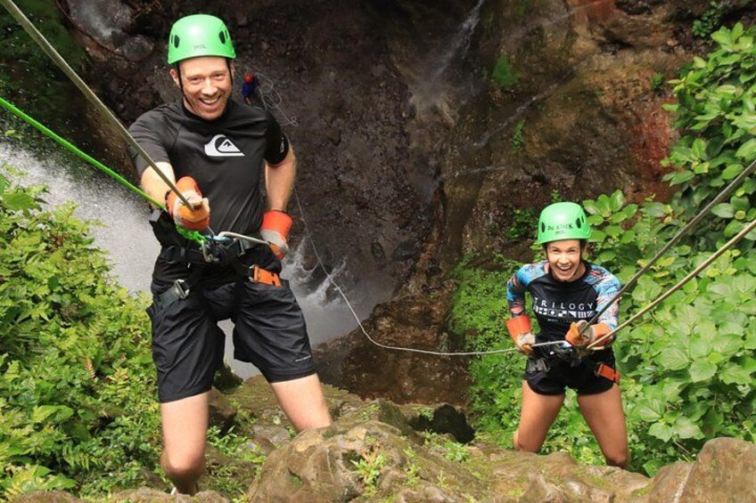 Two people rappelling down a rocky cliff with vegetation around. 5